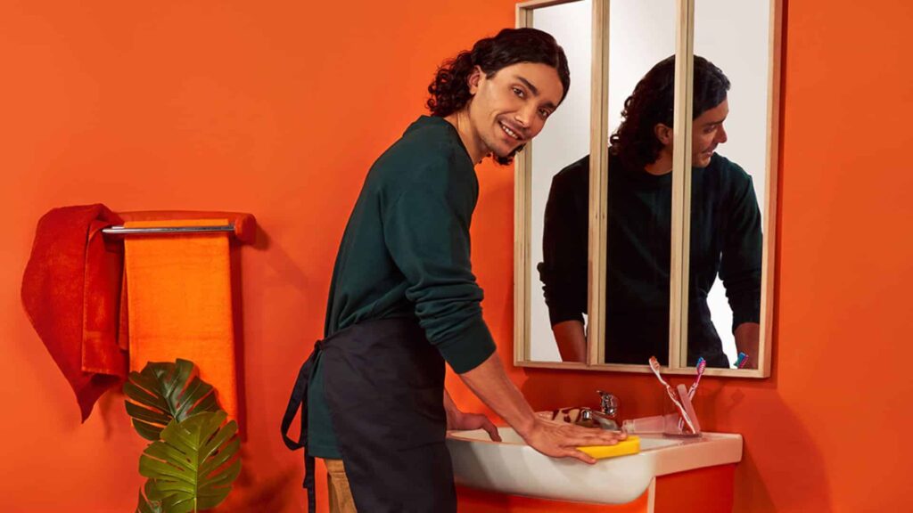 Un homme de ménage nettoie la salle de bains, le miroir et le lavabo