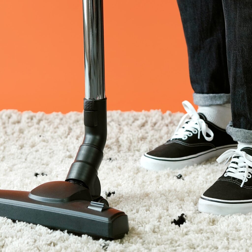 Quelqu'un passe l'aspirateur sur un tapis blanc.