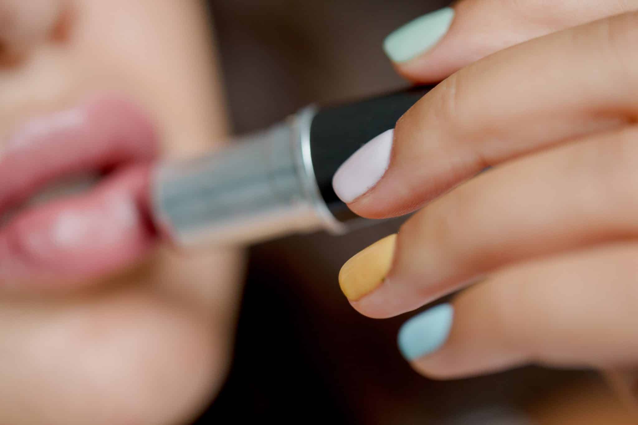 Une femme avec des ongles vernis et soignés s'applique du rouge à lèvres.